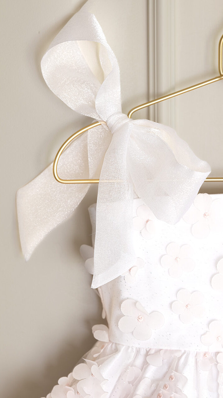 close-up of girls smocked bodice dress with bow straps and floral overlay, sewing pattern detail view