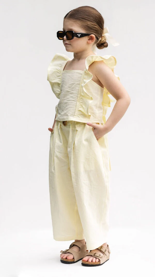 Child wearing unisex wide-leg cropped trousers with side pockets and elastic waist, paired with a girls ruffle tie-back top.