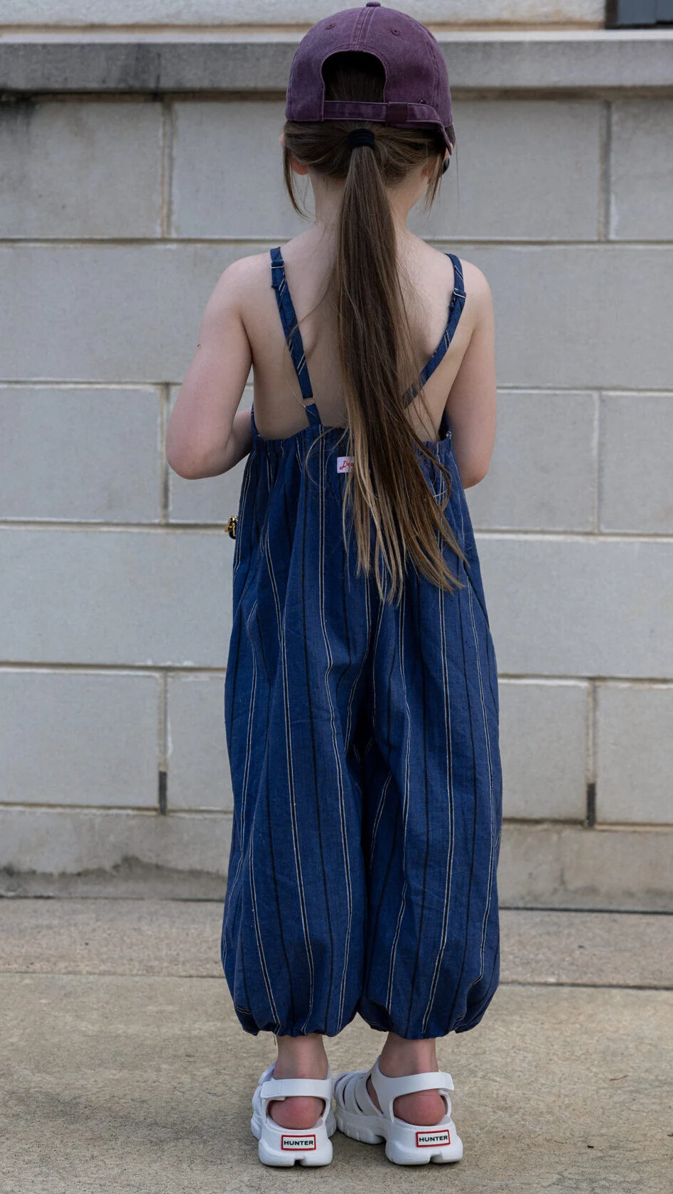 Back view of kids overalls sewing pattern showing adjustable straps with rings and sliders, elasticated back casing, and roomy balloon legs.